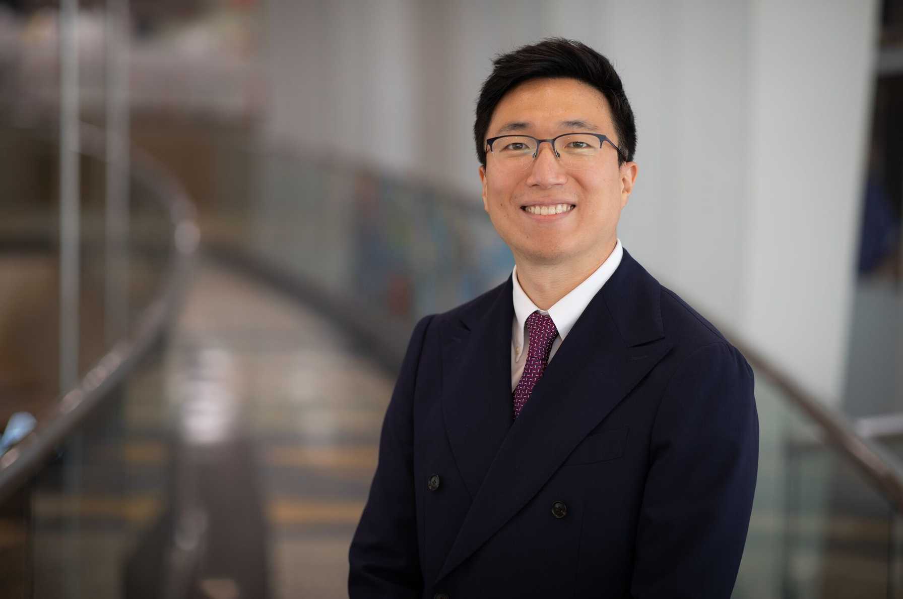Professional headshot of Hyun S. Kim, MD, Program Director, Interventional Pulmonology Fellowship, standing in a bright indoor hallway with glass railings.