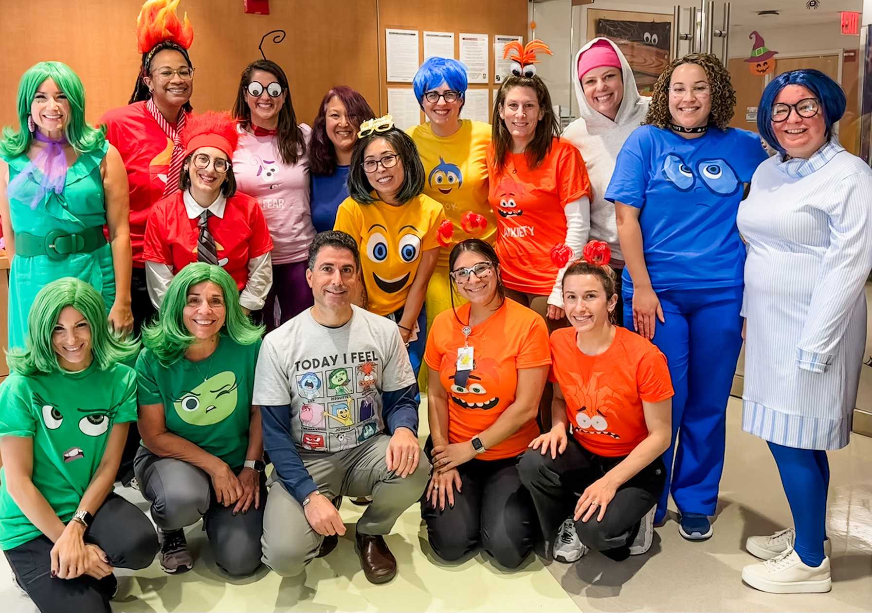 Group of staff dressed in colorful Inside Out-themed costumes posing together in a hospital hallway.
