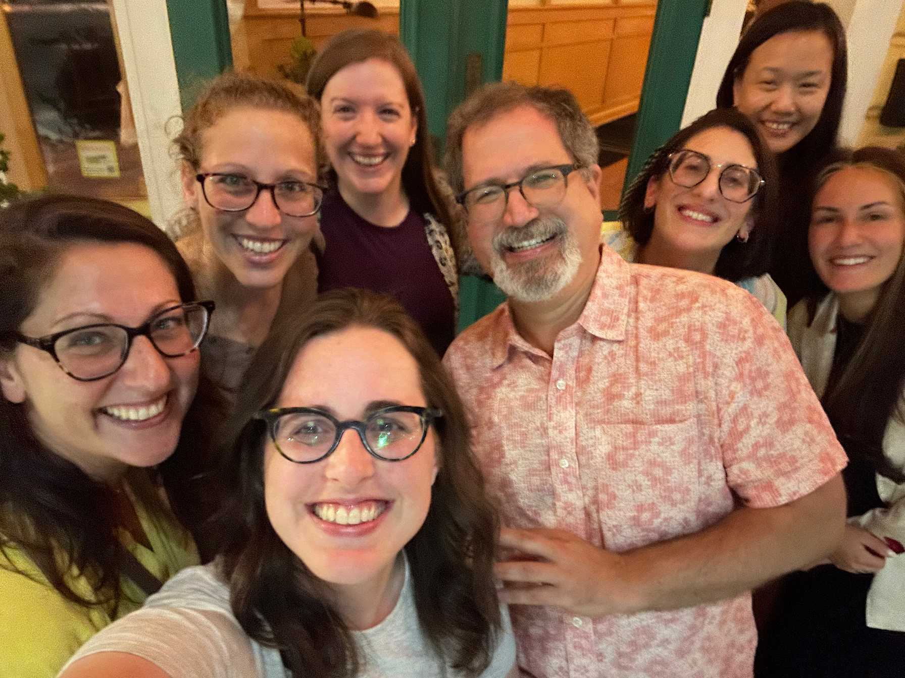 Group of smiling colleagues posing for a selfie indoors, with warm lighting and cheerful expressions.