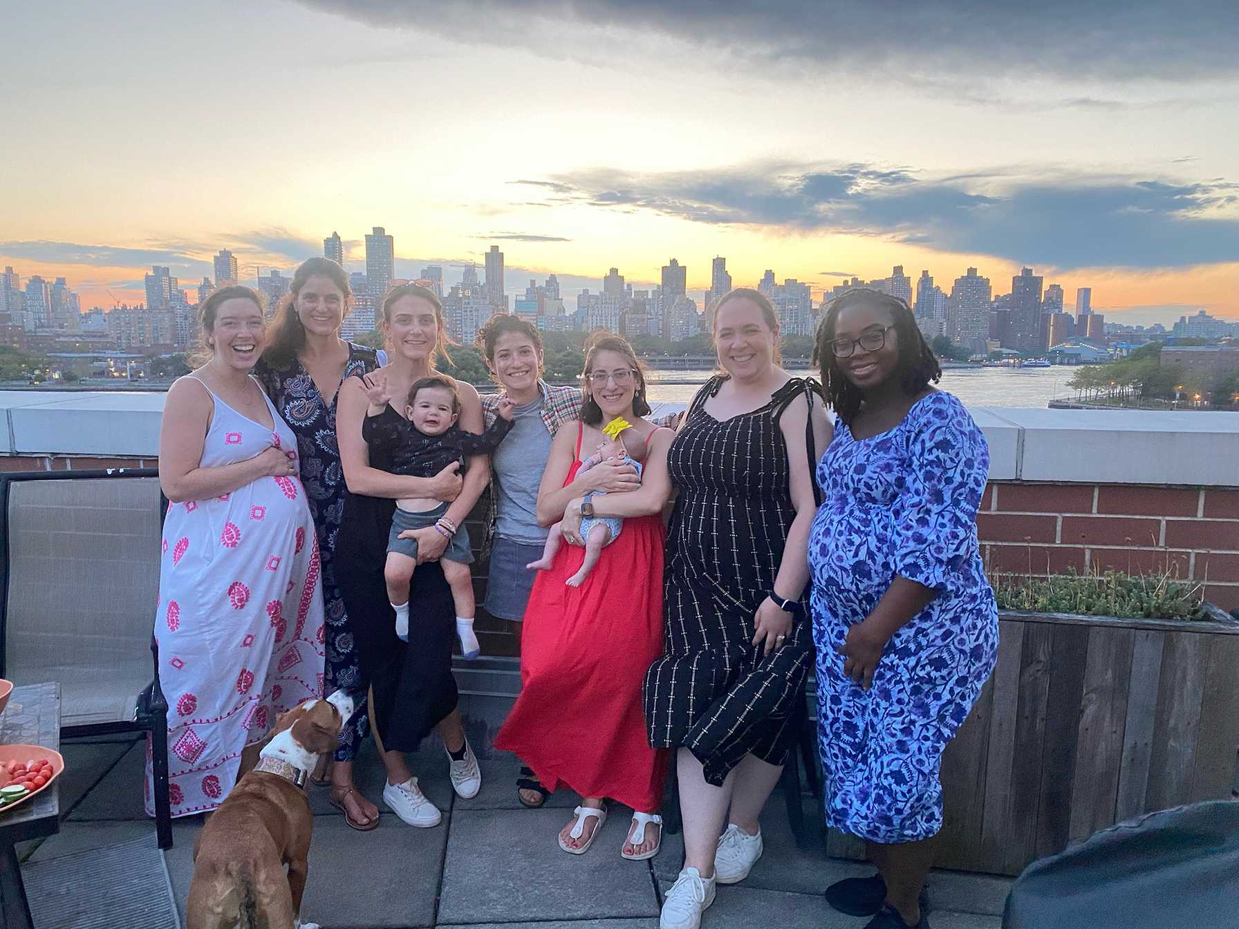 Group of women and children on a rooftop at sunset with a city skyline in the background.