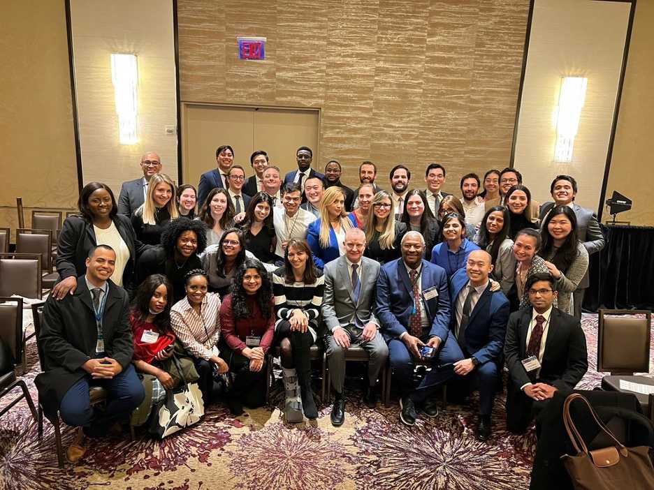 Large group of professionals dressed in business attire posing together at a conference in a hotel ballroom.