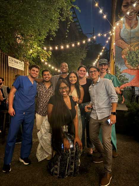 Group of friends gathered at an outdoor venue under string lights, smiling and enjoying the evening.
