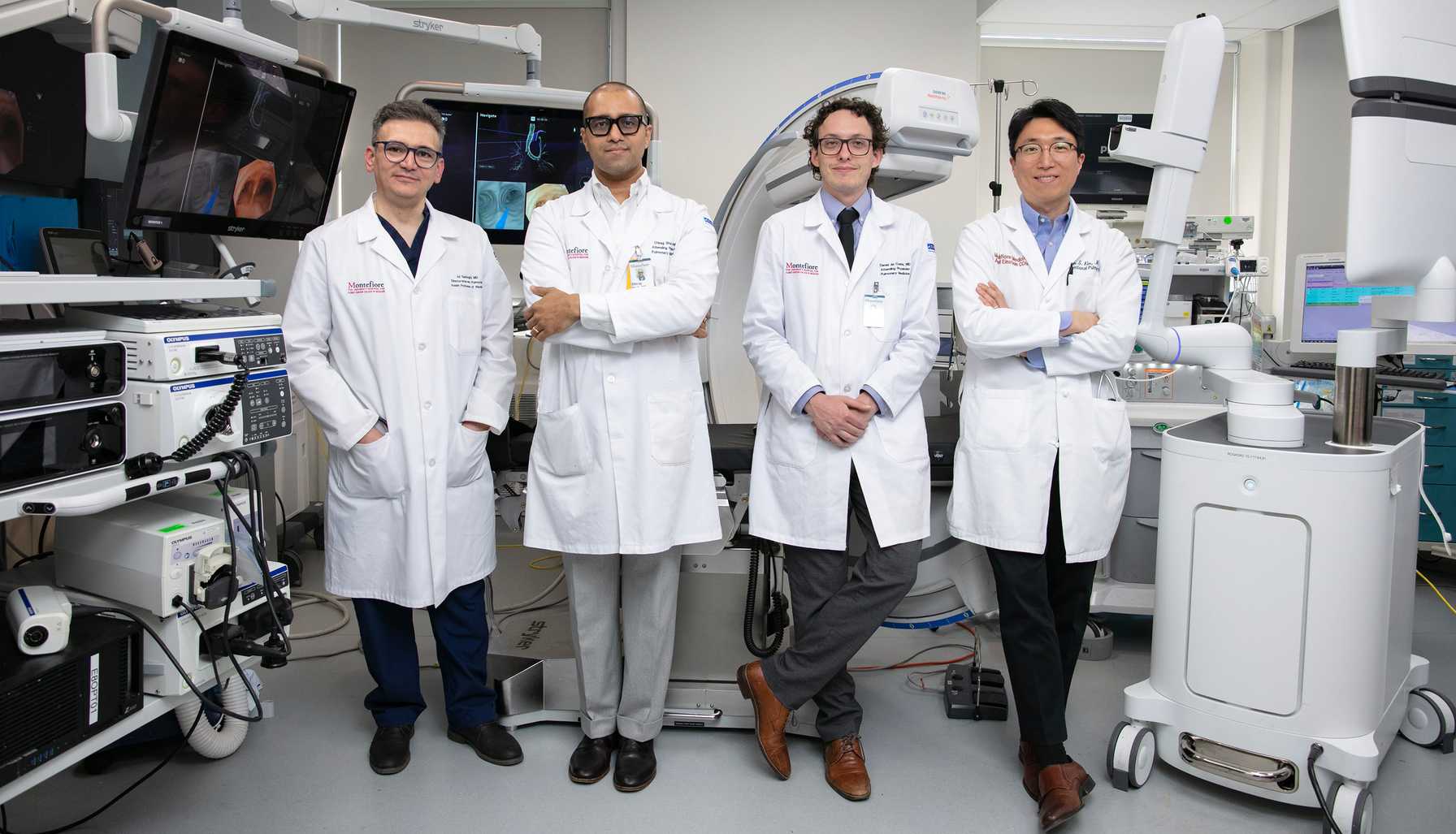 Four doctors in white lab coats standing in a high-tech interventional pulmonology suite with advanced medical imaging equipment.