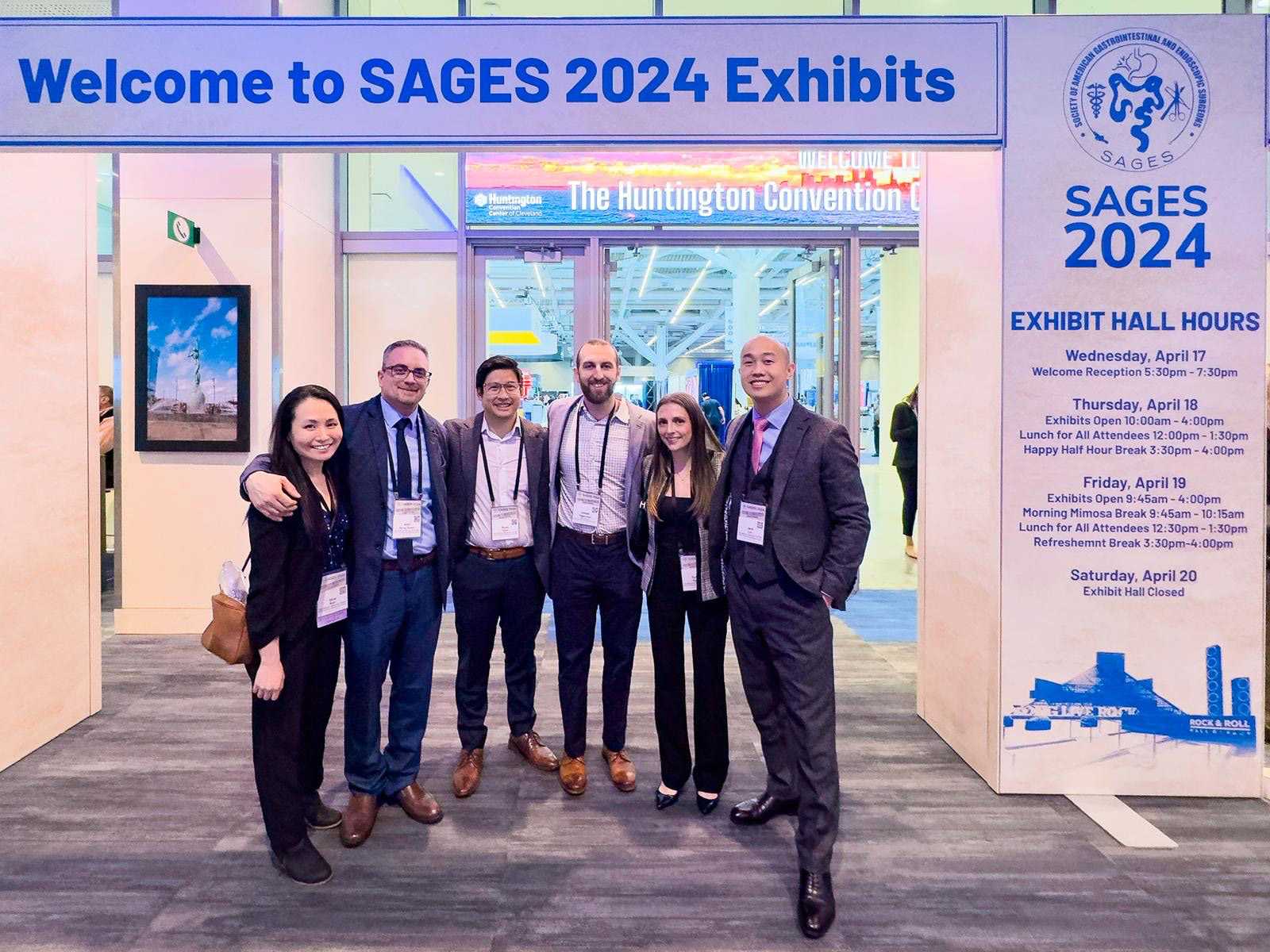 Group of professionals smiling and posing under a "Welcome to SAGES 2024 Exhibits" sign at a convention center entrance.