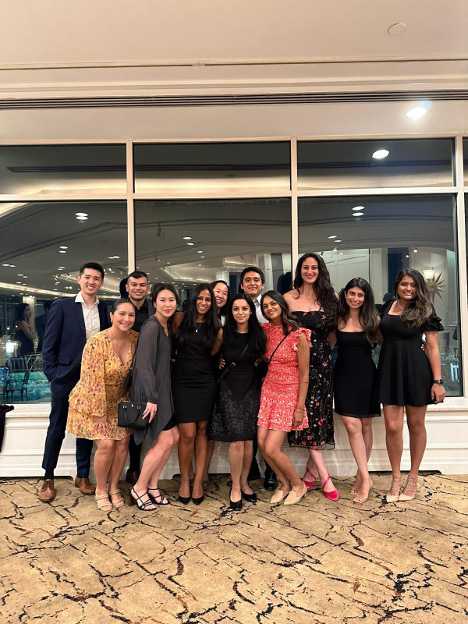 Group of young adults dressed in semi-formal outfits posing together at an indoor event.